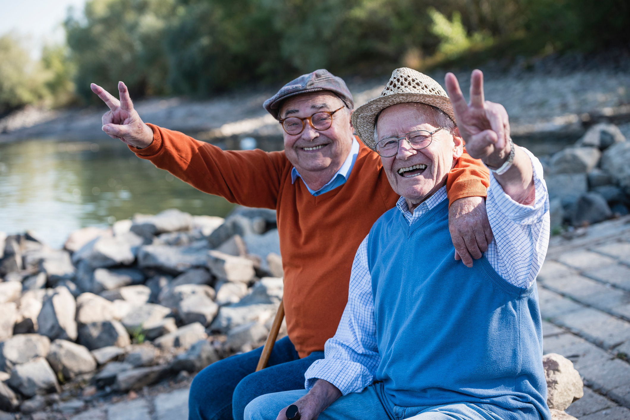 Zwei ältere Männer sitzen lachend am Rand eines Sees