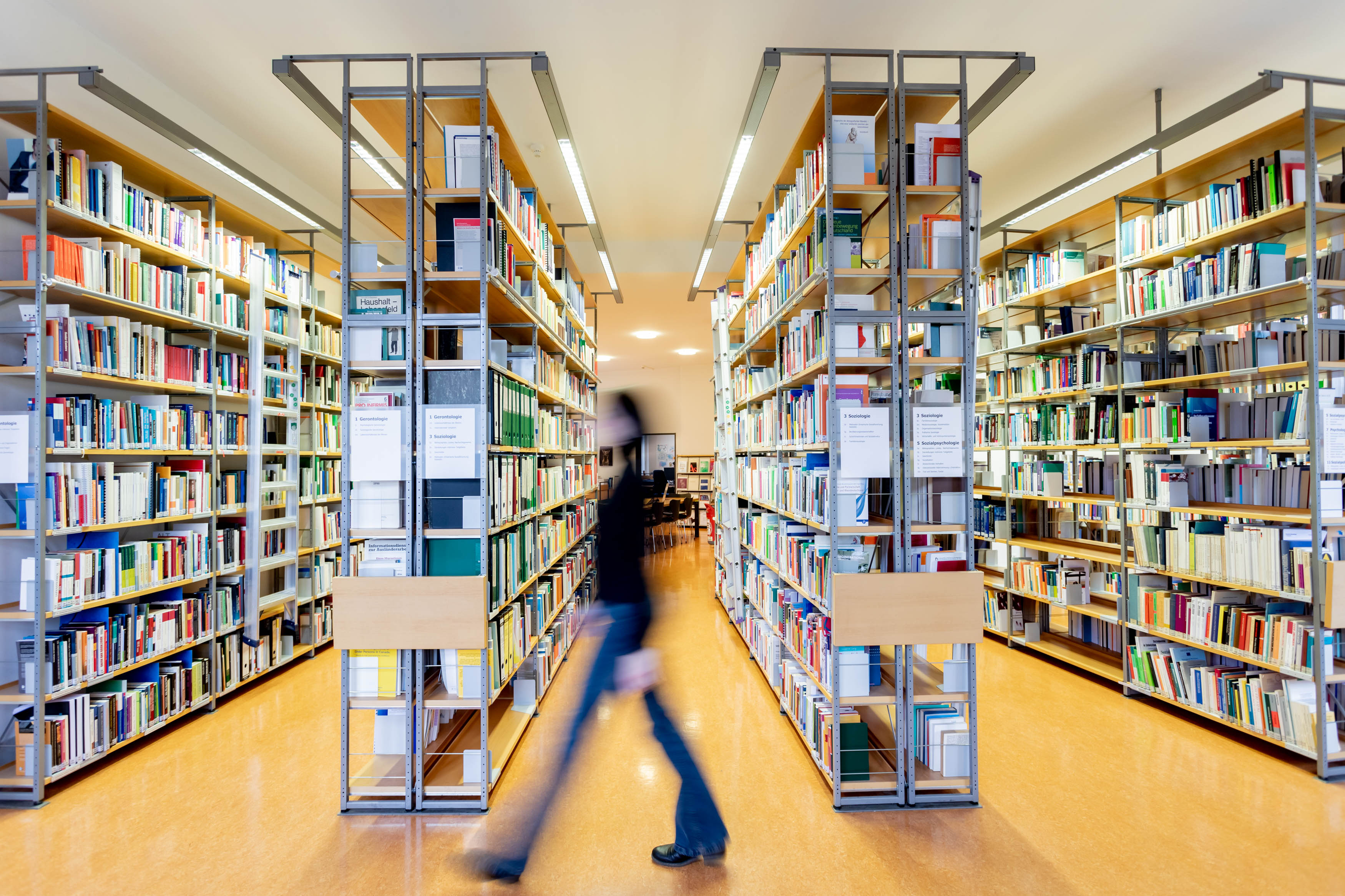 Das Foto zeigt Regale der DZA-Bibliothek und eine nur schemenhaft erkennbare Person, die daran vorbeigeht. Deutsches Zentrum für Altersfragen/Christoph Soeder